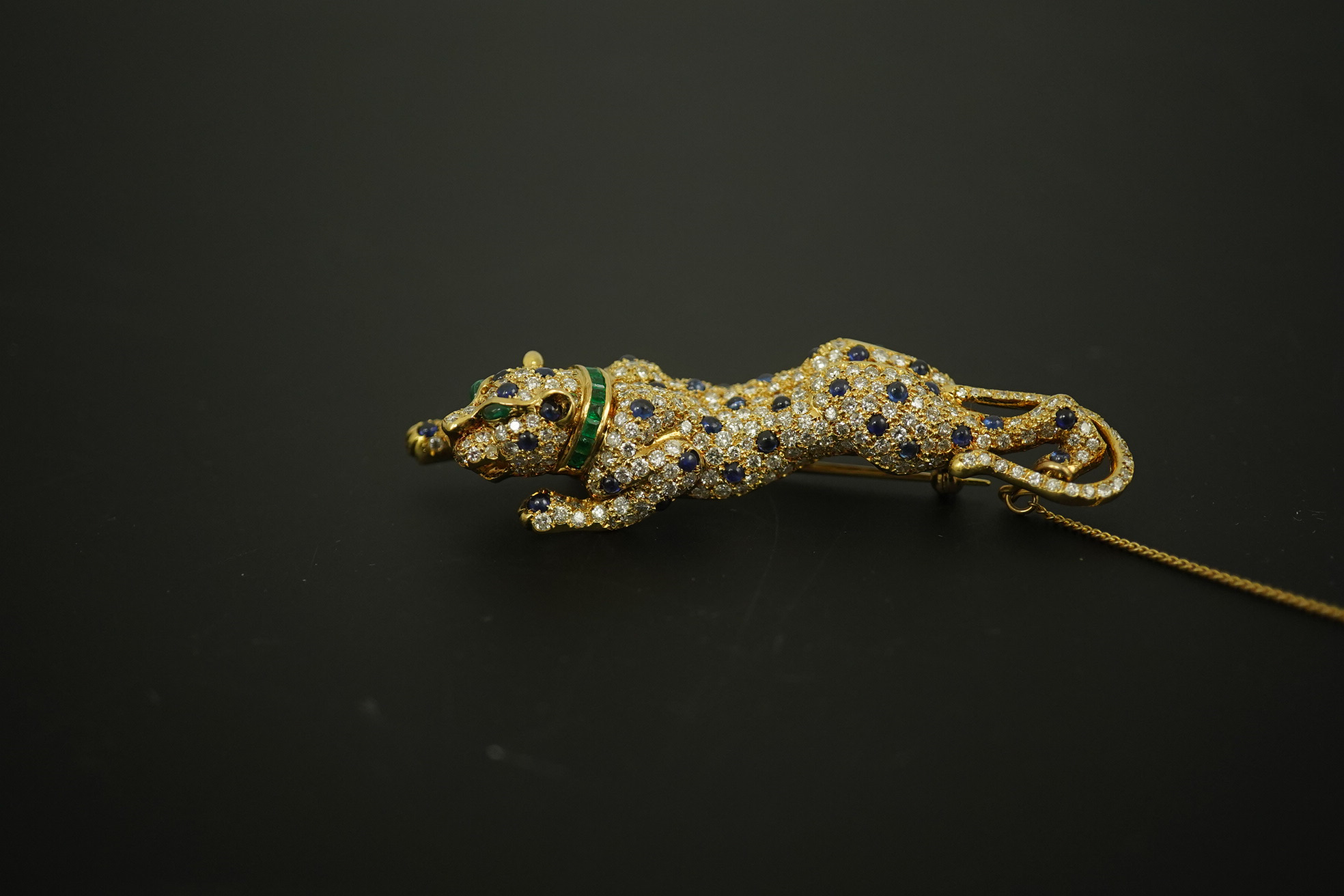 A modern Cartier style 18k gold, sapphire, emerald and diamond cluster set stalking panther brooch